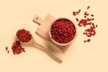 Ahşap kase ve kaşık, sarı arka planda kırmızı kurutulmuş goji üzümleri.