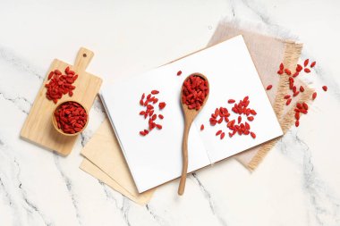 Ahşap kaşık ve kase, beyaz arka planda kırmızı kurutulmuş goji üzümleri.