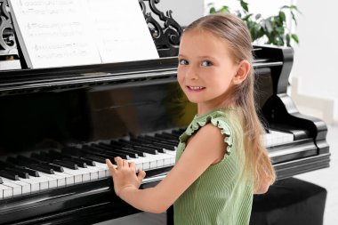 Cute little happy girl with notes playing grand piano at home