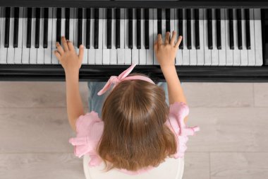 Cute little girl playing grand piano at home, top view