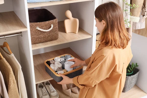 Young woman putting organizer with socks on shelf in wardrobe, back view