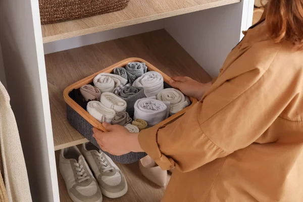 Young woman putting organizer with socks on shelf in wardrobe, closeup
