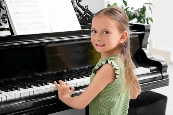 Cute little happy girl with notes playing grand piano at home
