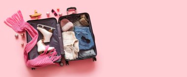 İçinde kışlık giysiler, buz patenleri ve pembe arka planda Noel dekoru olan bavulu aç.