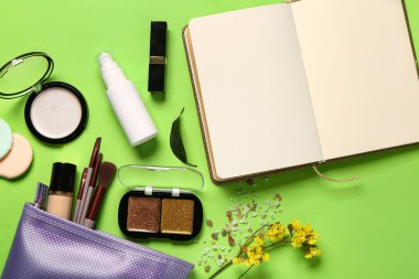 Makyaj malzemeleri, defter ve yeşil arka planda güzel çiçekler olan kozmetik çanta.