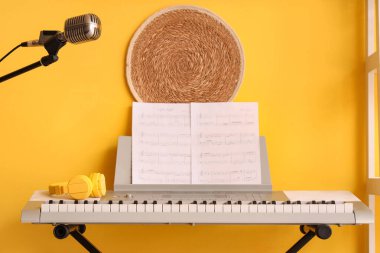 Sarı duvarın yanında nota kağıtları ve kulaklıkları olan modern sentezleyici.