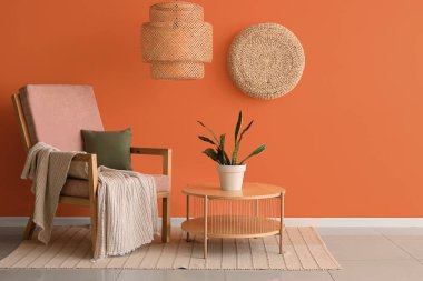 Oturma odasının içindeki turuncu duvarın yanındaki masa ve koltuk.