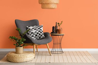 Pouf, masa ve koltuk turuncu duvarın yanında oturma odasının içinde.