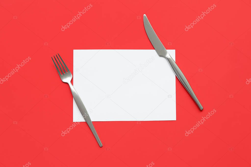 Blank card, stainless steel fork and knife on red background