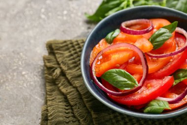 Gri arka planda kırmızı soğan ve fesleğen yapraklı taze domates salatası. Yakın plan.
