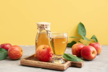 Gri masada meyveli bir şişe ve bir bardak taze elma şarabı.