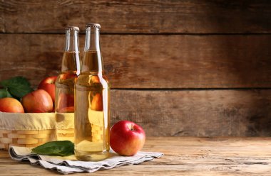 Taze elma şarabı şişeleri ve ahşap arka planda meyveler.