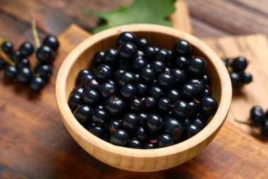Ahşap arka planda taze siyah üzümlü kase, yakın plan.