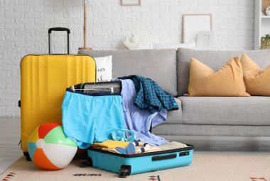 İçinde erkek mayosu, plaj topu ve şnorkelli maske olan bavulu oturma odasında aç.