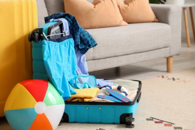 İçinde erkek mayosu, plaj topu ve şnorkelli maske olan bavulu oturma odasında aç.