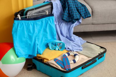 İçinde erkek mayosu, plaj topu ve şnorkelli maske olan bavulu aç.