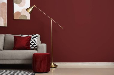 Kırmızı duvarın yanında rahat gri kanepesi ve standart lambası olan şık bir oturma odası.