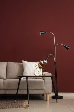 Şık oturma odasının içinde rahat gri kanepe, sehpa ve kırmızı duvarın yanında standart lamba.