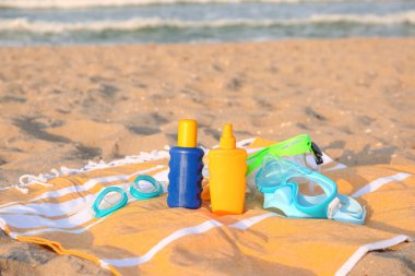 Plaj aksesuarları ve kumdaki güneş kremi şişeleriyle.