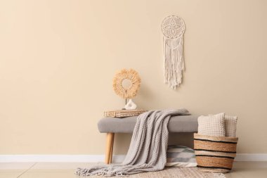 Saf battaniyeli gri bank, bej duvarın yanında kitaplar ve sepet.