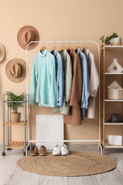 Bej duvarın yanında giysi askılığı ve raf ünitesi olan modern soyunma odasının içinde.