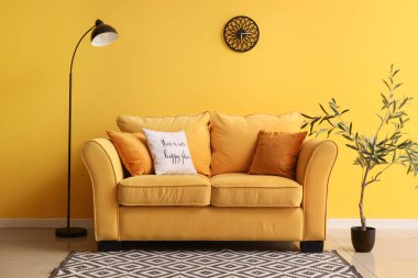 Rahat bir kanepe, zemin lambası ve oturma odasının içinde dekoratif zeytin ağacı.