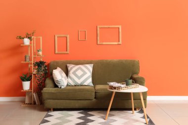 Rahat bir kanepe ve oturma odasının iç tarafındaki turuncu duvarın yanındaki masa.