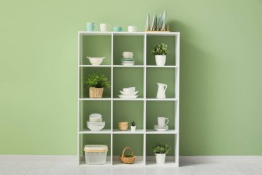 Mutfağın içinde temiz bulaşık takımları ve ev bitkileri olan raf ünitesi.