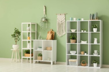 Mutfağın içinde temiz bulaşık takımları ve ev bitkileri olan raflar.