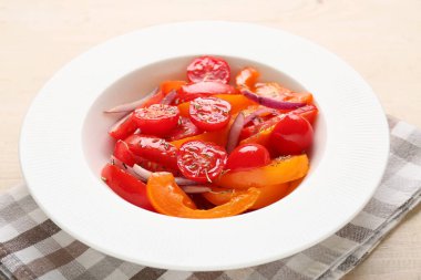 Bej ahşap arka planda kırmızı soğanlı taze domates salatası, yakın plan.