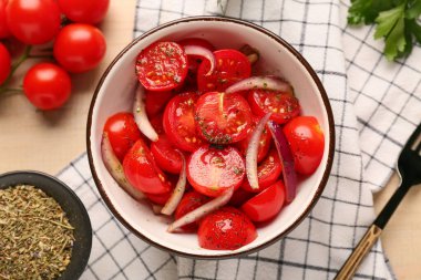 Bej ahşap arka planda kırmızı soğanlı bir kase taze domates salatası.