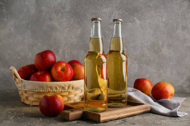 Taze elma şarabı şişeleri ve gri arka planda meyveler.