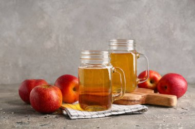 Mason kavanozları dolusu taze elma şarabı ve gri arka planda meyveler.