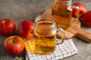 Mason kavanozları dolusu taze elma şarabı ve gri arka planda meyveler, yakın plan.