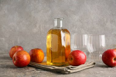 Bir şişe taze elma şarabı ve gri arka planda meyveler.