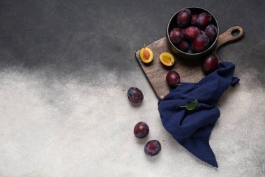 Koyu arkaplanda taze olgun erikler olan bir kase ve ahşap tahta.