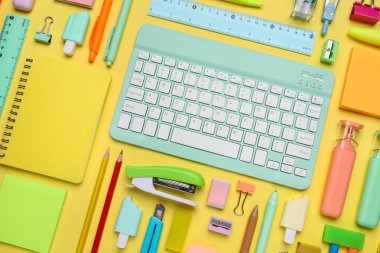 Sarı arka planda bilgisayar klavyeli okul gereçleri, yakın plan