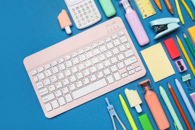 Mavi arkaplanda bilgisayar klavyesi olan okul malzemeleri seti, yakın plan