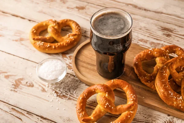 Bir bardak soğuk bira ve beyaz ahşap arka planda lezzetli krakerler, yakın plan.