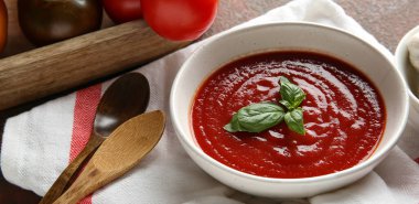 Bir kase taze domates çorbası ve arka planda taze sebzeler.