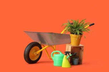 Turuncu arka planda bitki, bahçe aletleri ve el arabası.