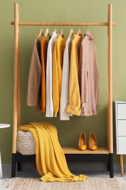 Soyunma odasındaki yeşil duvarın yanında kazak, topuklu ayakkabı ve puf var.