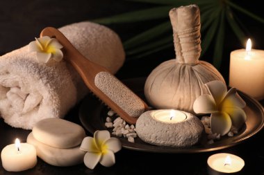 Bitkisel çantalı tepsi, çiçekler, sünger taşı ve siyah arka planda yanan mumlar, yakın plan