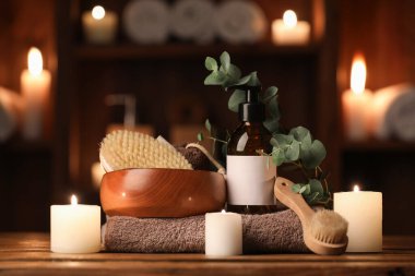 Bir şişe kozmetik ürünü, oda odasındaki ahşap masada yanan mumlar ve banyo malzemeleri.