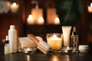 Kozmetik ürünleri şişeleri, lif süngeri ve karanlık odadaki ahşap masada yanan mumlar.