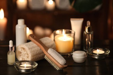 Kozmetik ürünleri şişeleri, lif süngeri ve karanlık odadaki ahşap masada yanan mumlar.