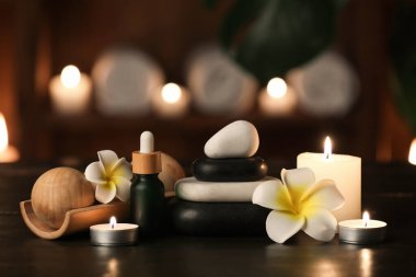 Spa taşları, kozmetik ürünleri, masaj topları, çiçekler ve karanlık odadaki ahşap masada yanan mumlar.