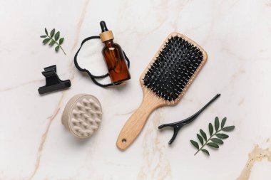 Saç fırçası, kozmetik ürün şişesi ve bej mermer arka planda yeşil yapraklı kompozisyon