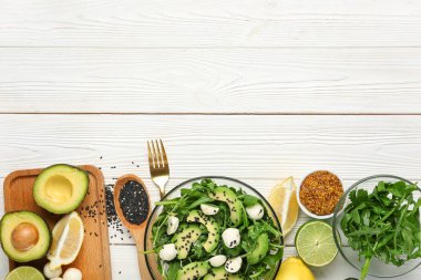 Sağlıklı roka salatası ve beyaz ahşap arka planda malzemelerle dolu bir kase.