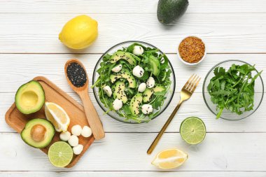 Sağlıklı roka salatası ve beyaz ahşap arka planda malzemelerle dolu bir kase.